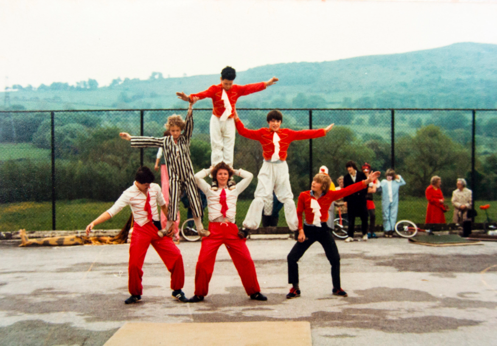 A circus act, a pyramid made of 6 people. They are all wearing red and white, and some people are wearing black too.