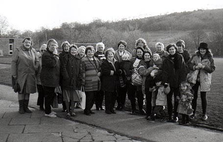 A black and white photo of a group of women stood smiling at the camera.