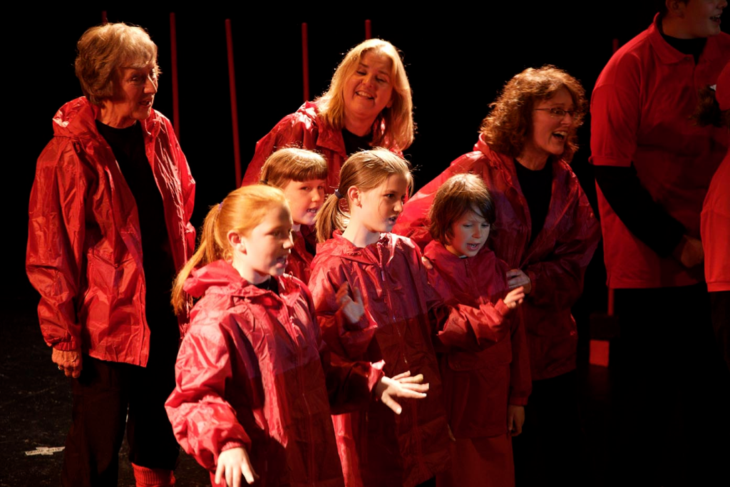 A group of adults and children all wearing red coats singing.