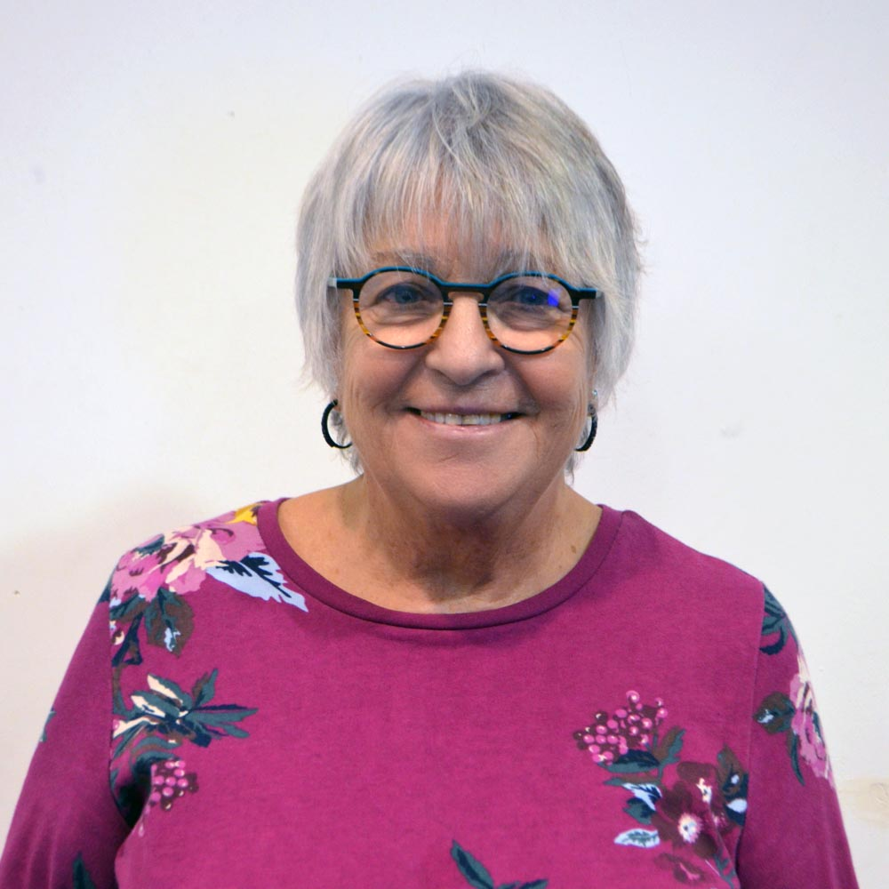 A woman with round glasses wearing a pink floral top.