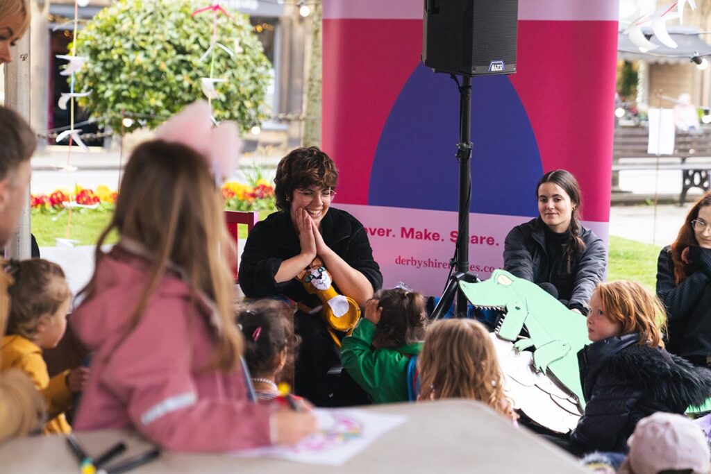 People sat with a young audience in front of them. On stage, the people are holding a cat and a dinosaur.