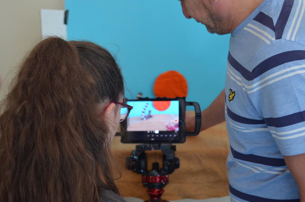 A girl looking at an iPad with a man to the right of her, showing her how to make an animation.