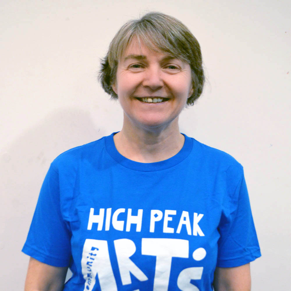 A woman smiling, wearing a blue High Peak Community Arts t-shirt.