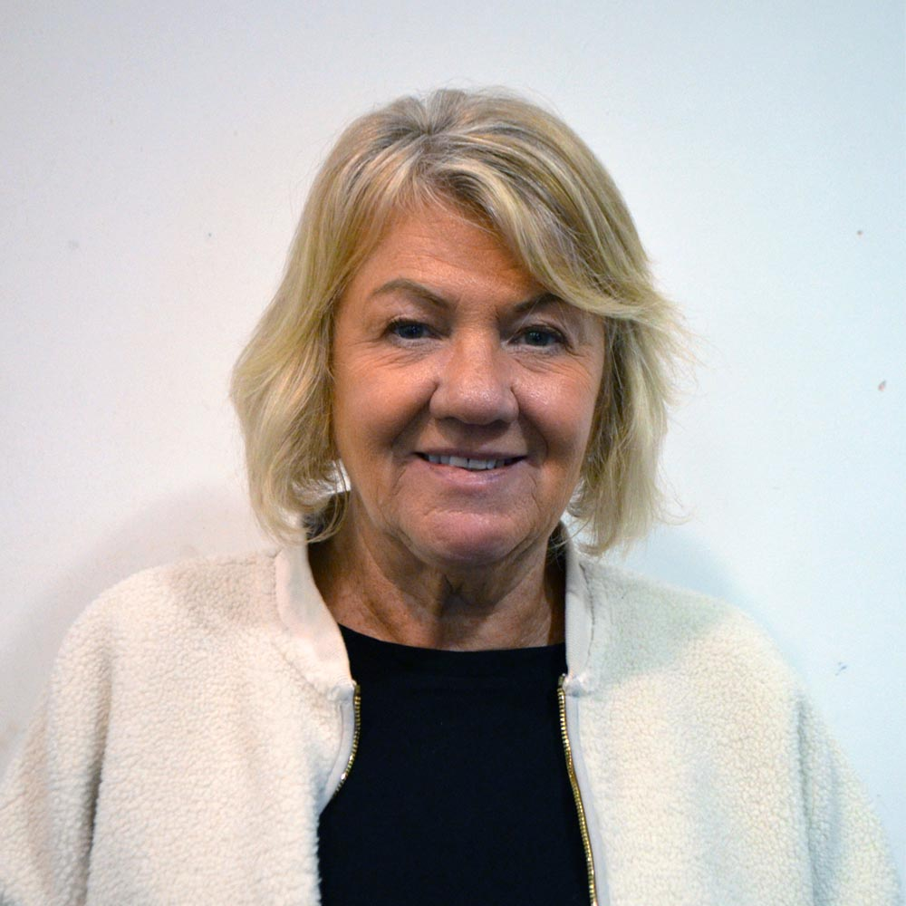A woman with blonde short hair wearing a black top and cream zipped jumper.