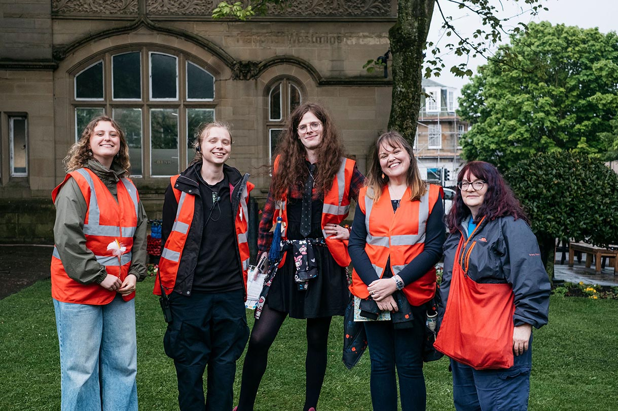 a group of volunteers with their volunteer coordinator smiling, wearing high-visability jackets