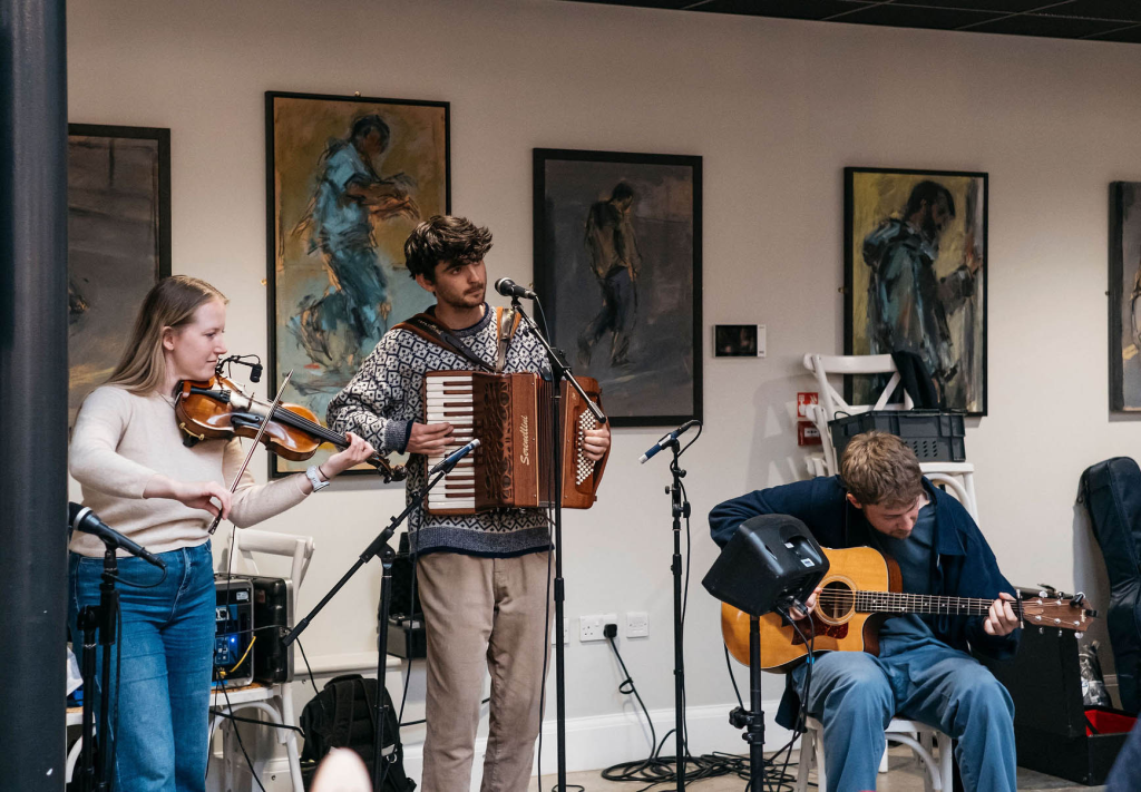 Three band members playing folk instruments with art behind