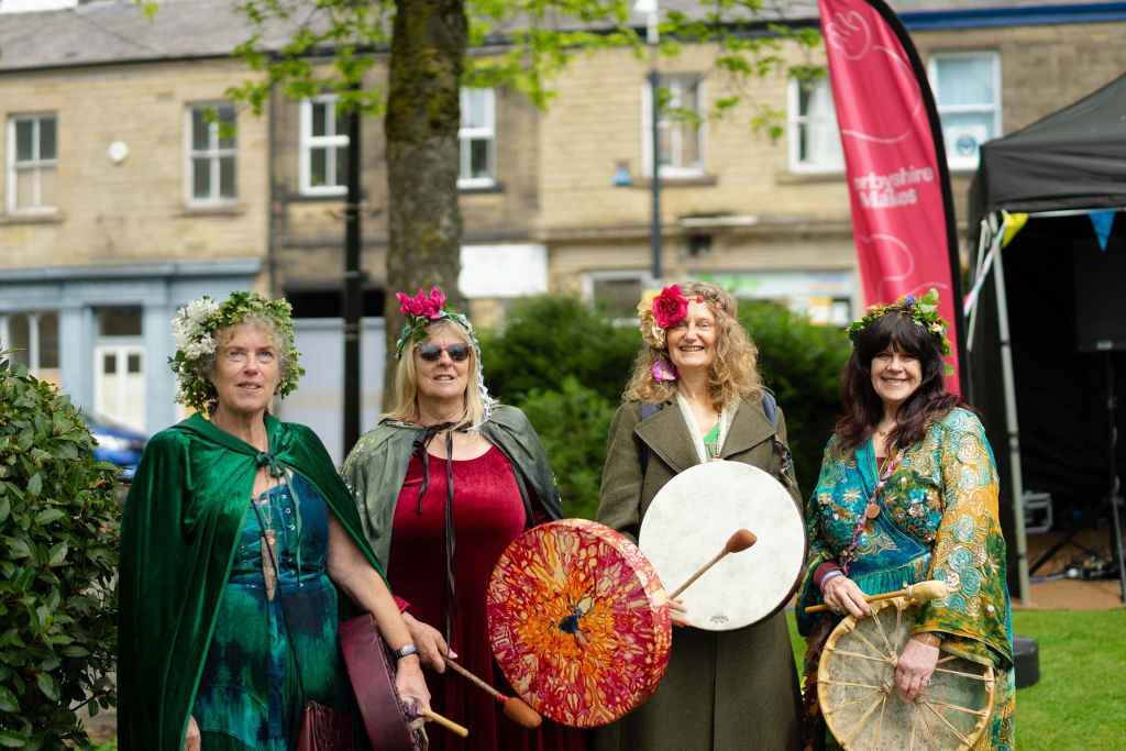 four females dressed in summer clothes and capes holding drums at a festival