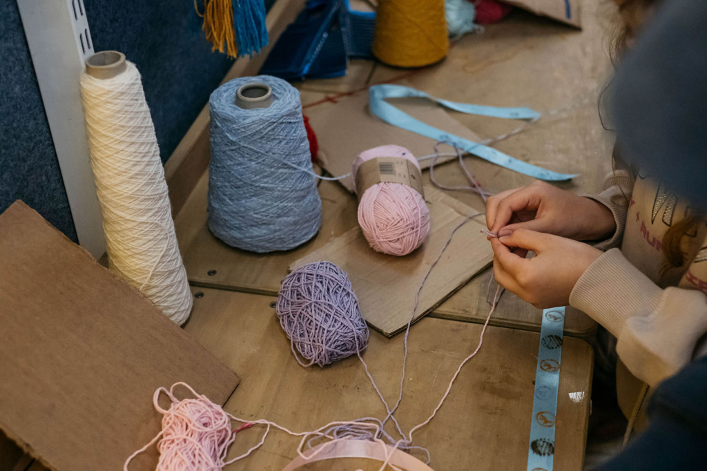hands threading a needle with pink, blue and purple thread