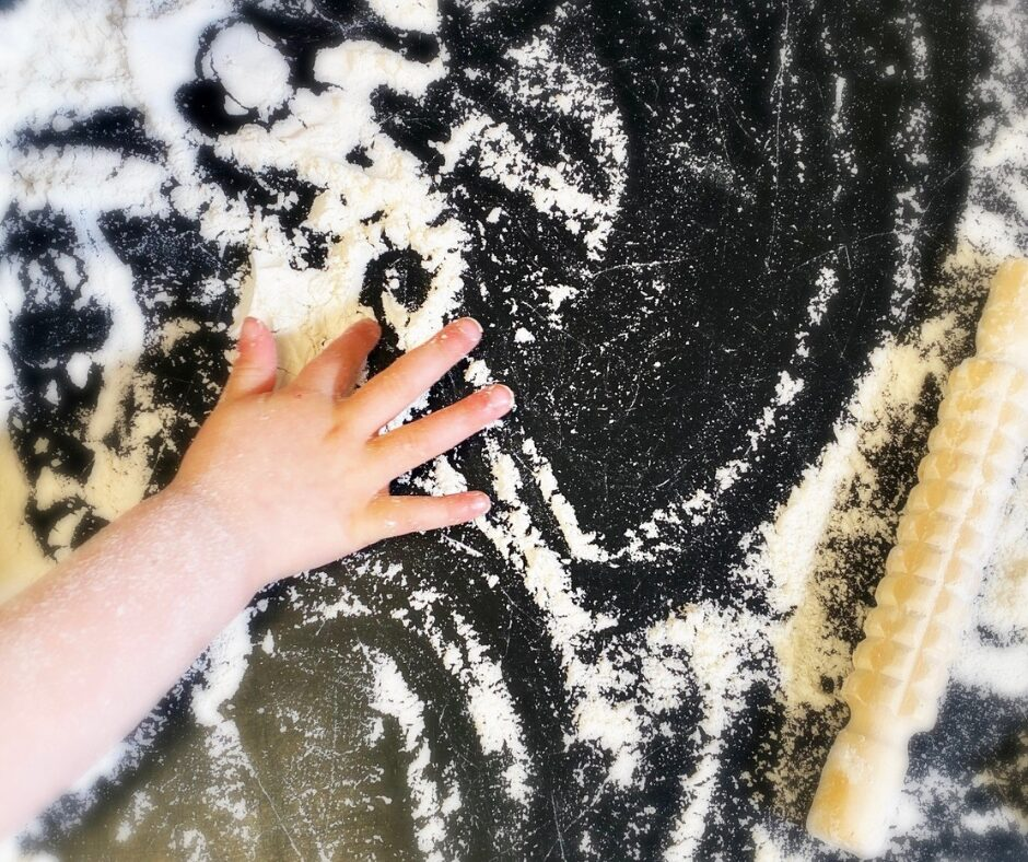 A young child's hand in a sensory play experience involving flour.