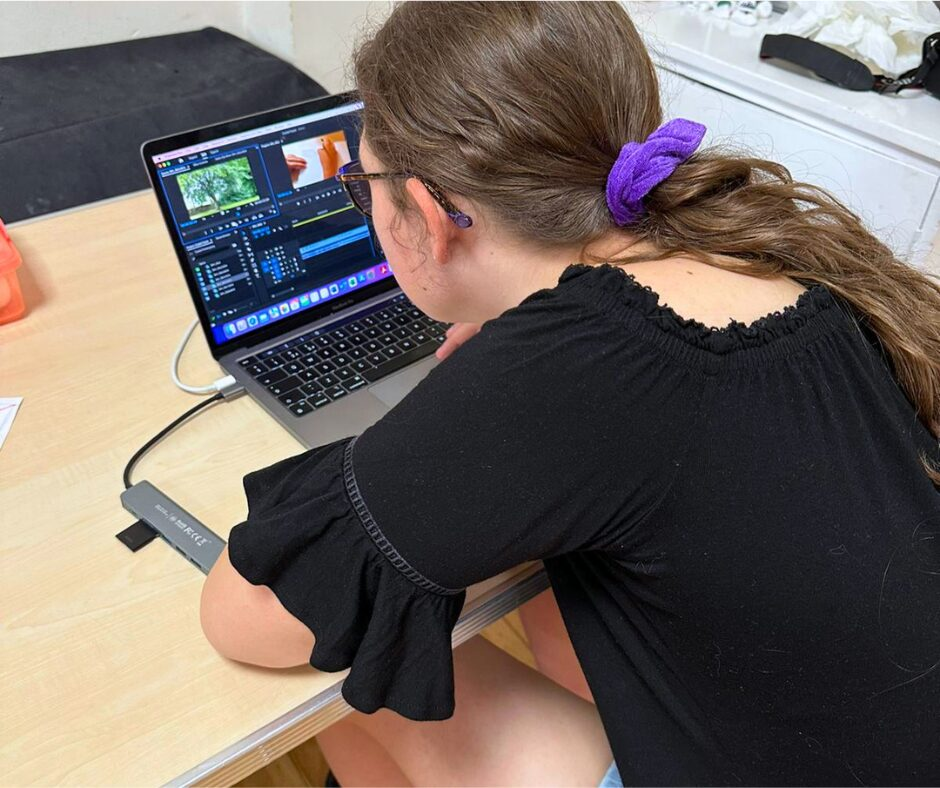 A young woman with her hair tied up looking at a MacBook with the editing software "Premiere Pro".