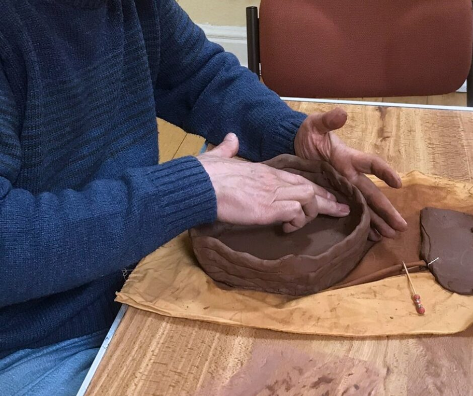 2 hands sculpting brown clay into a bowl-like shape.