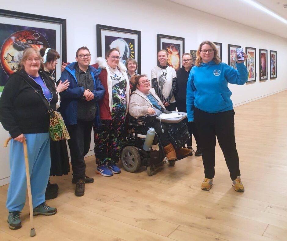 A group of people smiling infront of an art exhibition.