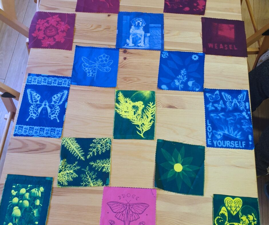 A table with cyanotype-printed images arranged in a pattern; the images include nature themes, a dog and a flower.