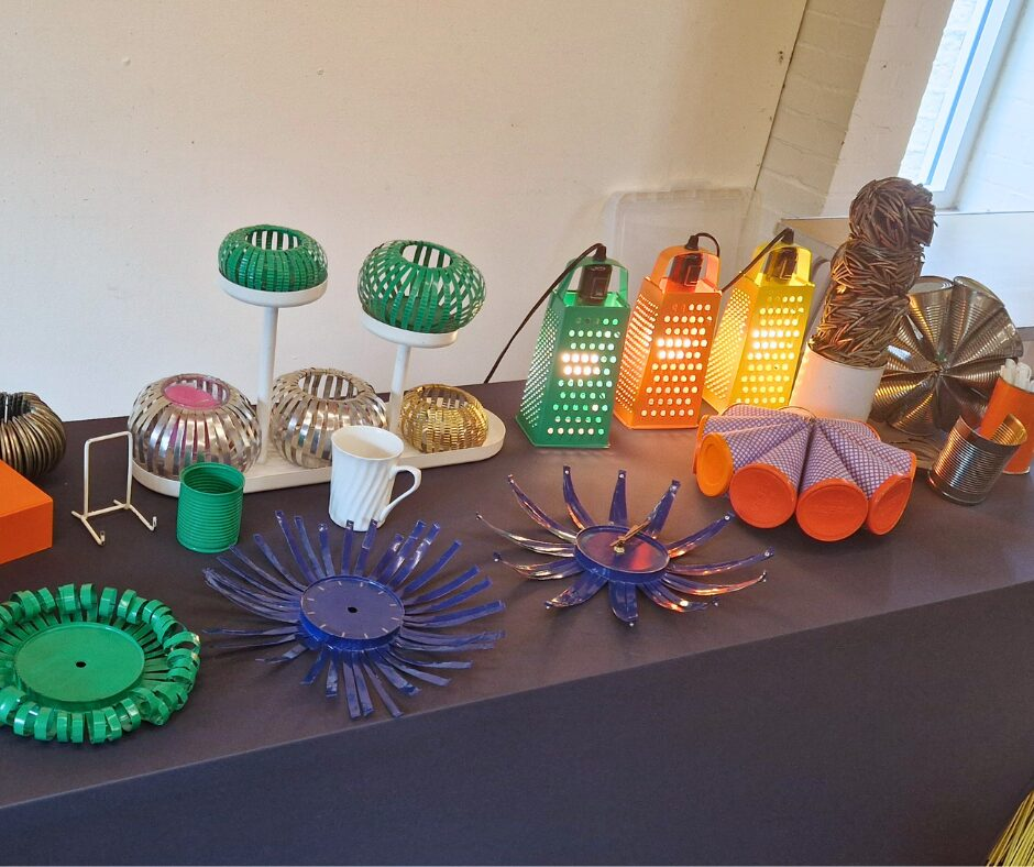 A table with upcycled projects including coloured cheese graters turned into lights and a decorative metal flowers crafted from a repurposed tin can.