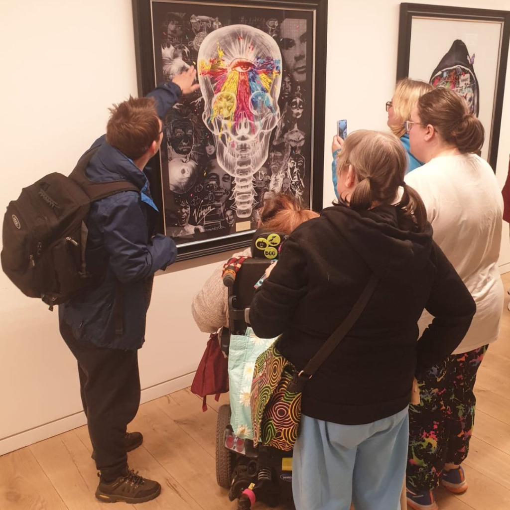A group of people looking at a piece of artwork that features a skull with different colours and faces in the background.